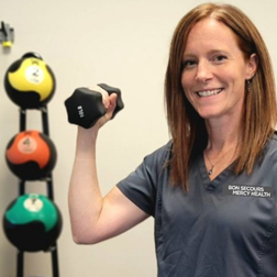 Physical therapist Marguerite K. in scrubs holding a dumbbell in a therapy gym