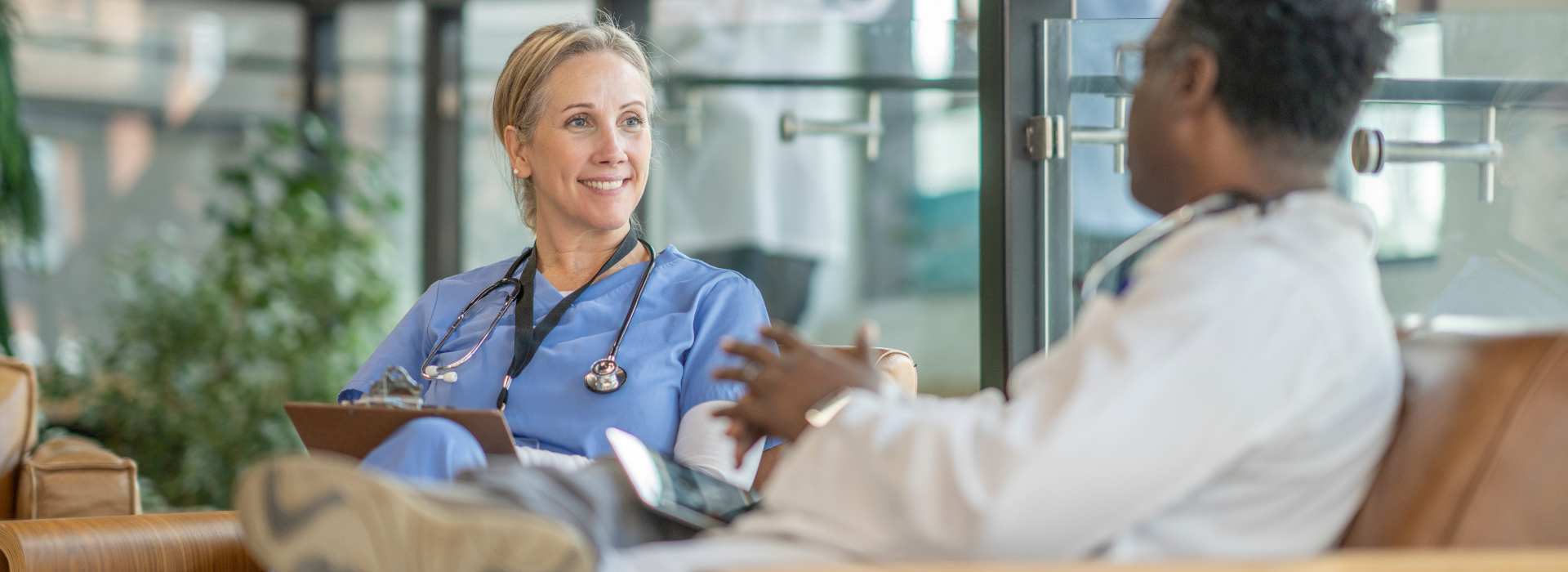 Two medical professionals sitting and talking to one another in a hospital setting women in scrubs man in white lab coat