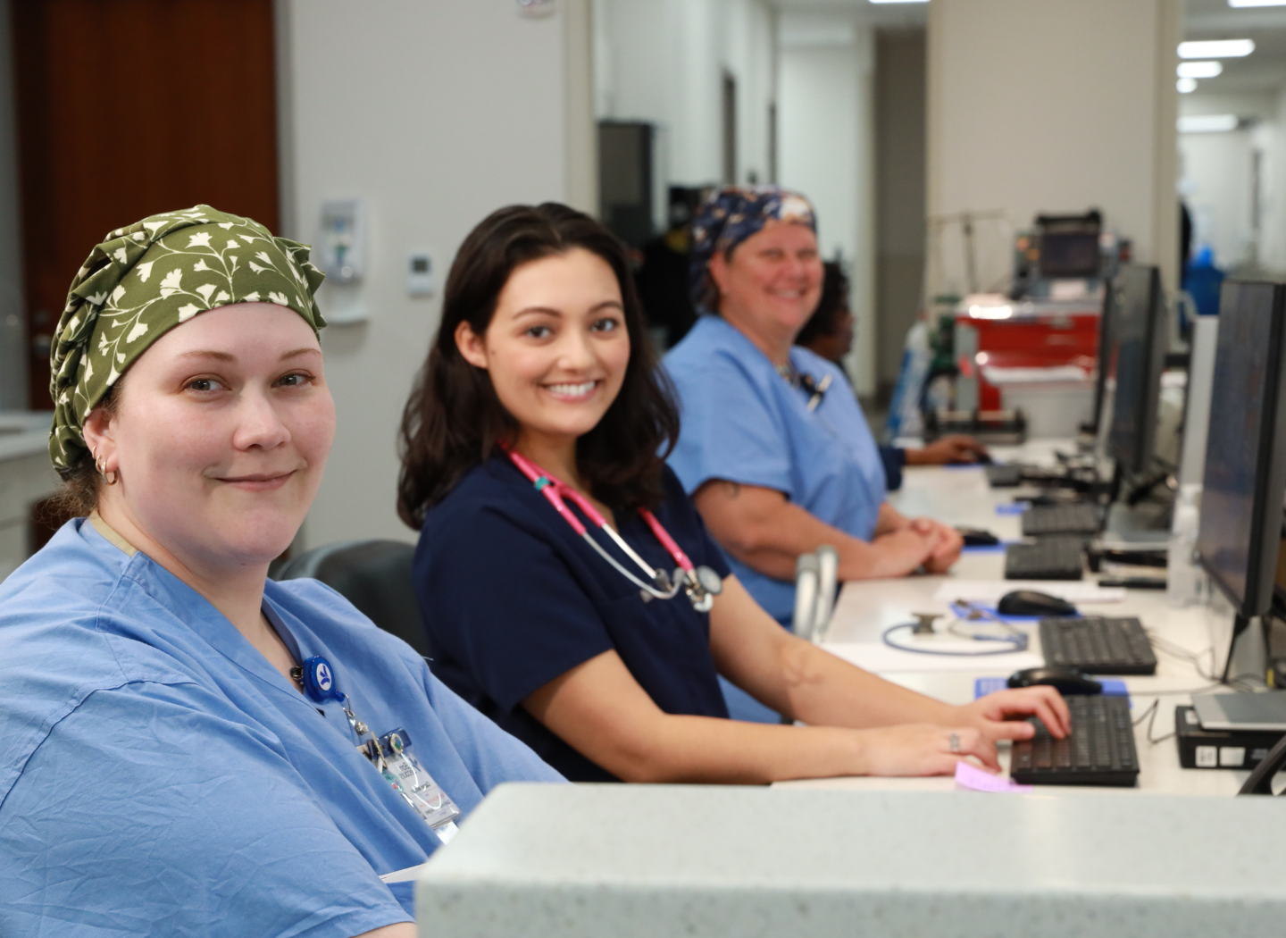 Three nurses at work station in light blue and dark blue scrubs