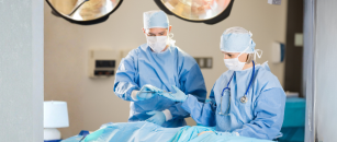 Two surgical professionals in protective attire work together during a procedure in an operating room.