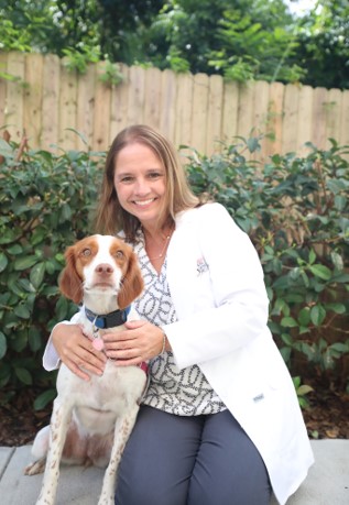 A smiling vet in a white lab coat crouches next to a tan and white dog. 