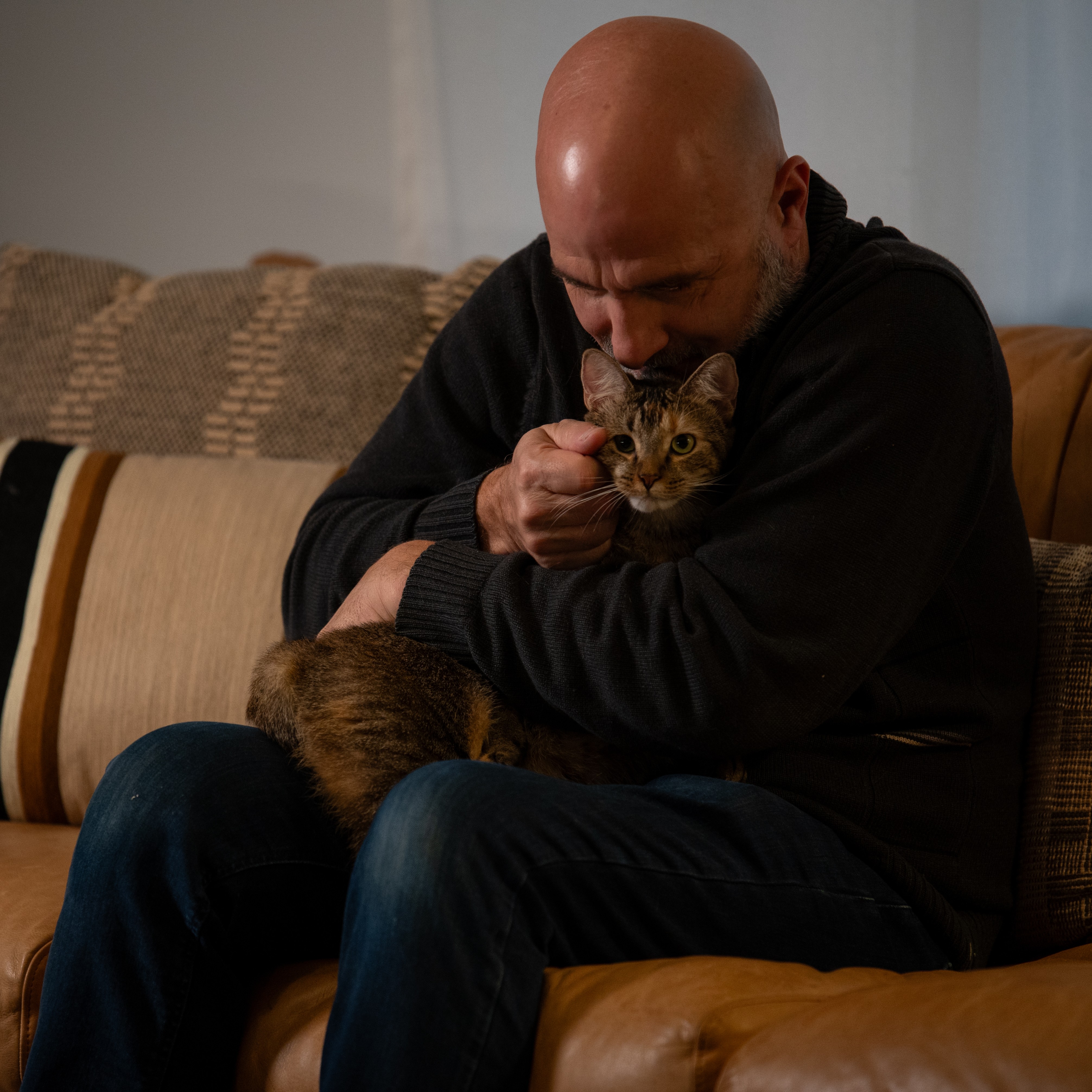 A bald man gives a hug and kiss to a calico cat.