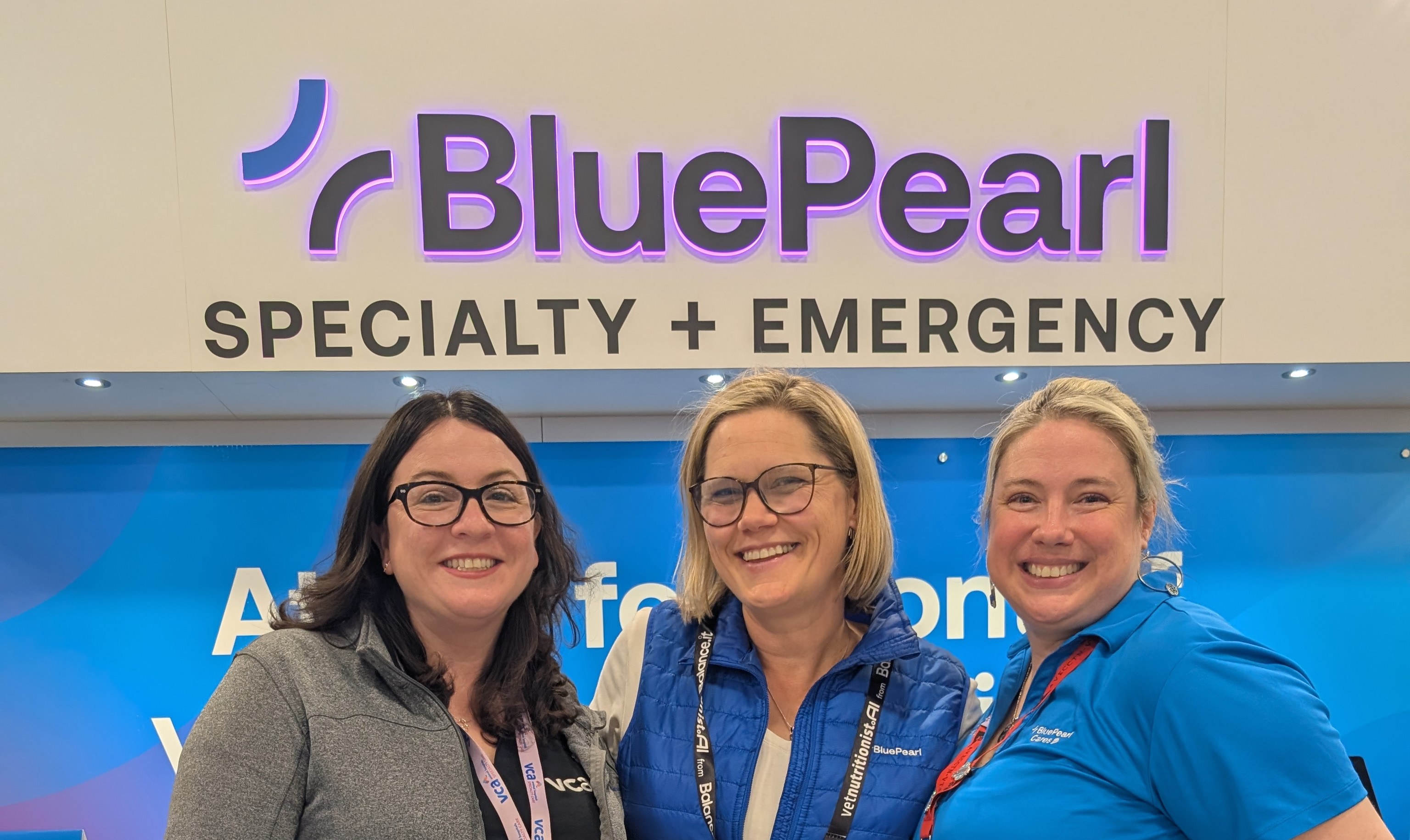 Three smiling BluePearl Associates, two wearing blue and one in gray, stand in front of their booth at ACVIM Forum 2026.