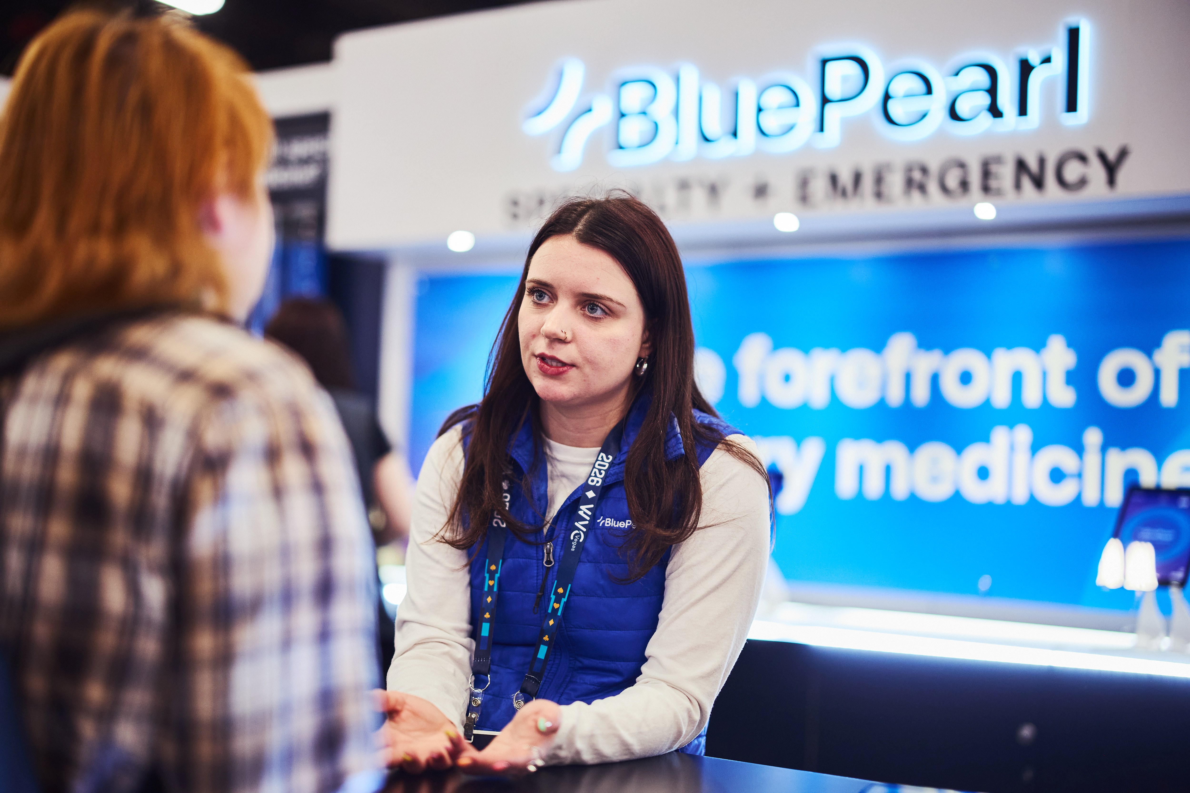 A BluePearl Associate chats with a visitor in a plaid shirt in front of the BluePearl booth.