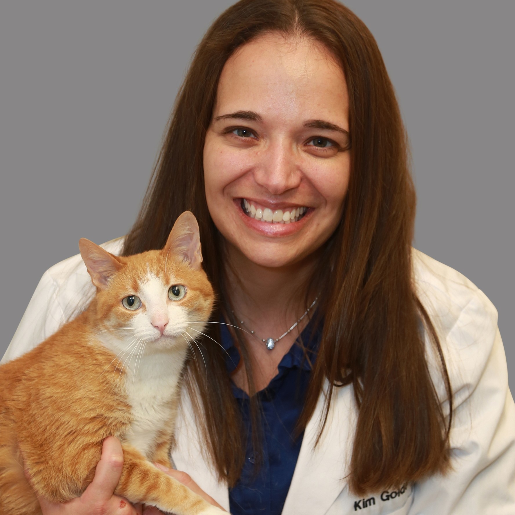 A BluePearl veterinarian with long brown hair, holding a happy orange cat.