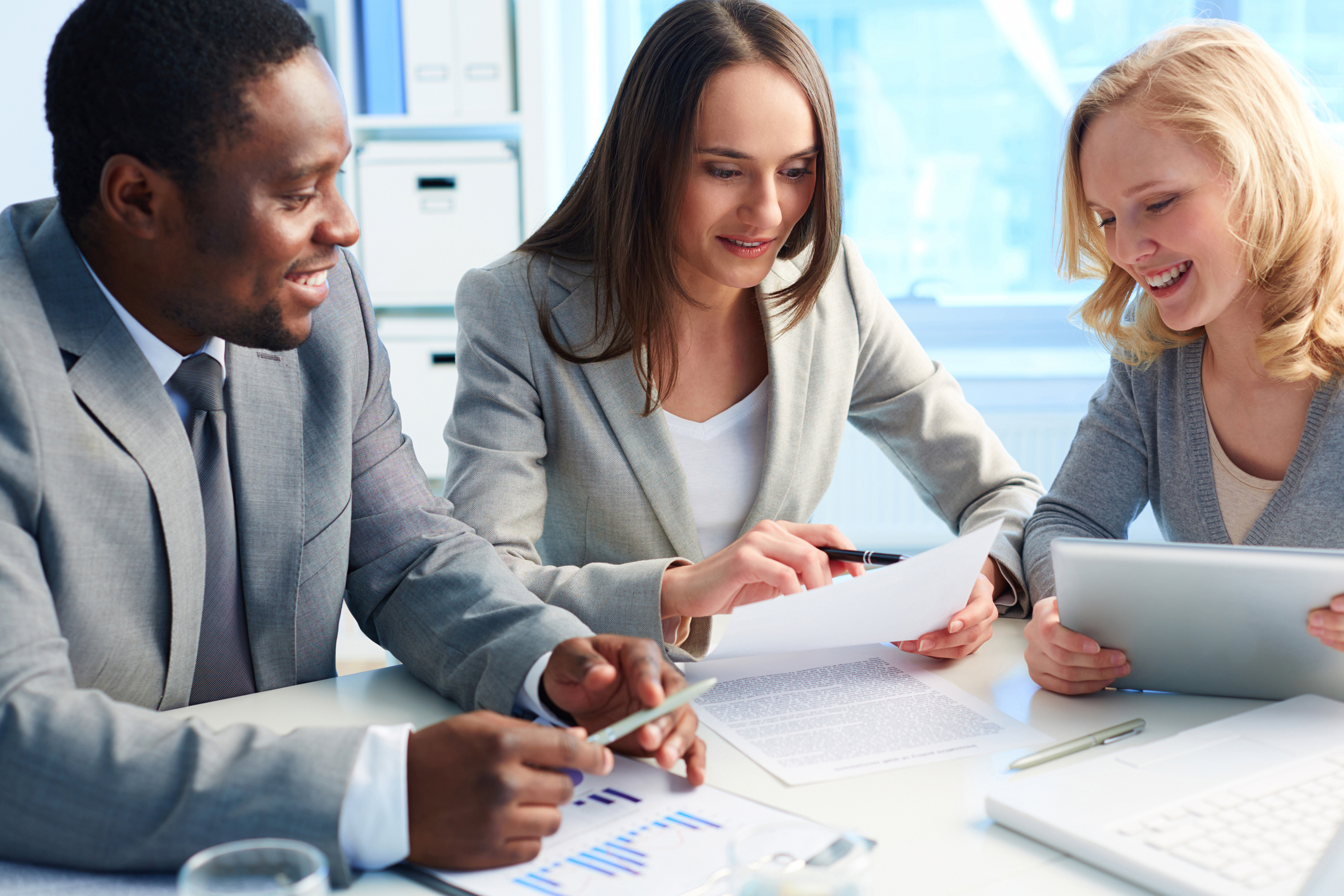 two women and one man sitting at desk looking at document