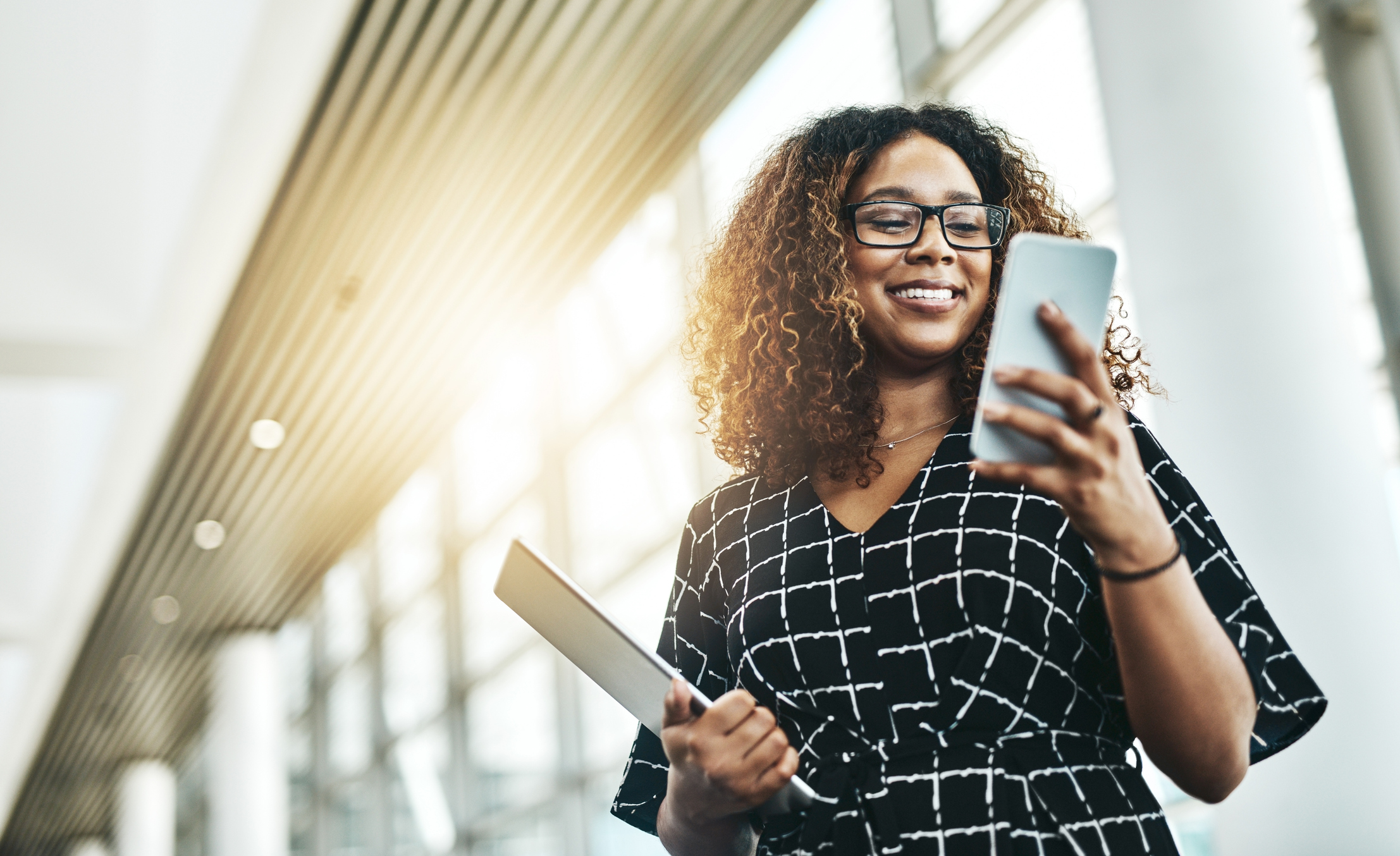 Woman smiling while looking at phone and holding tablet