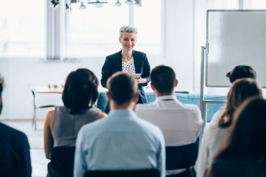 a woman giving a presentation in front of people who are sitting down