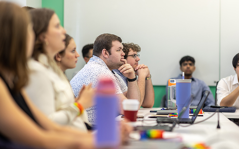 A group of Cencora interns are seated in a conference room at the Cencora Headquarters. They are listening to a presentation and have laptops open in front of them.