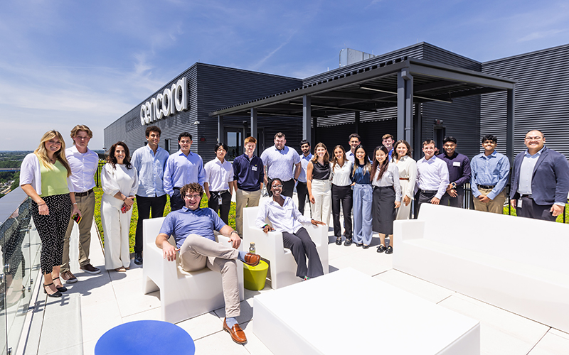 A large group of Cencora interns are gathered up on the rooftop terrace of Cencora's headquarters building. Some are sitting in chairs while several others are standing behind them. 