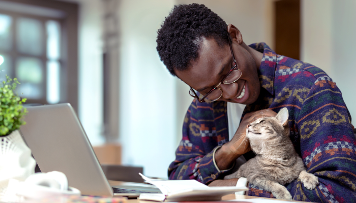 A man smiles as he pats his cat while working on his laptop.