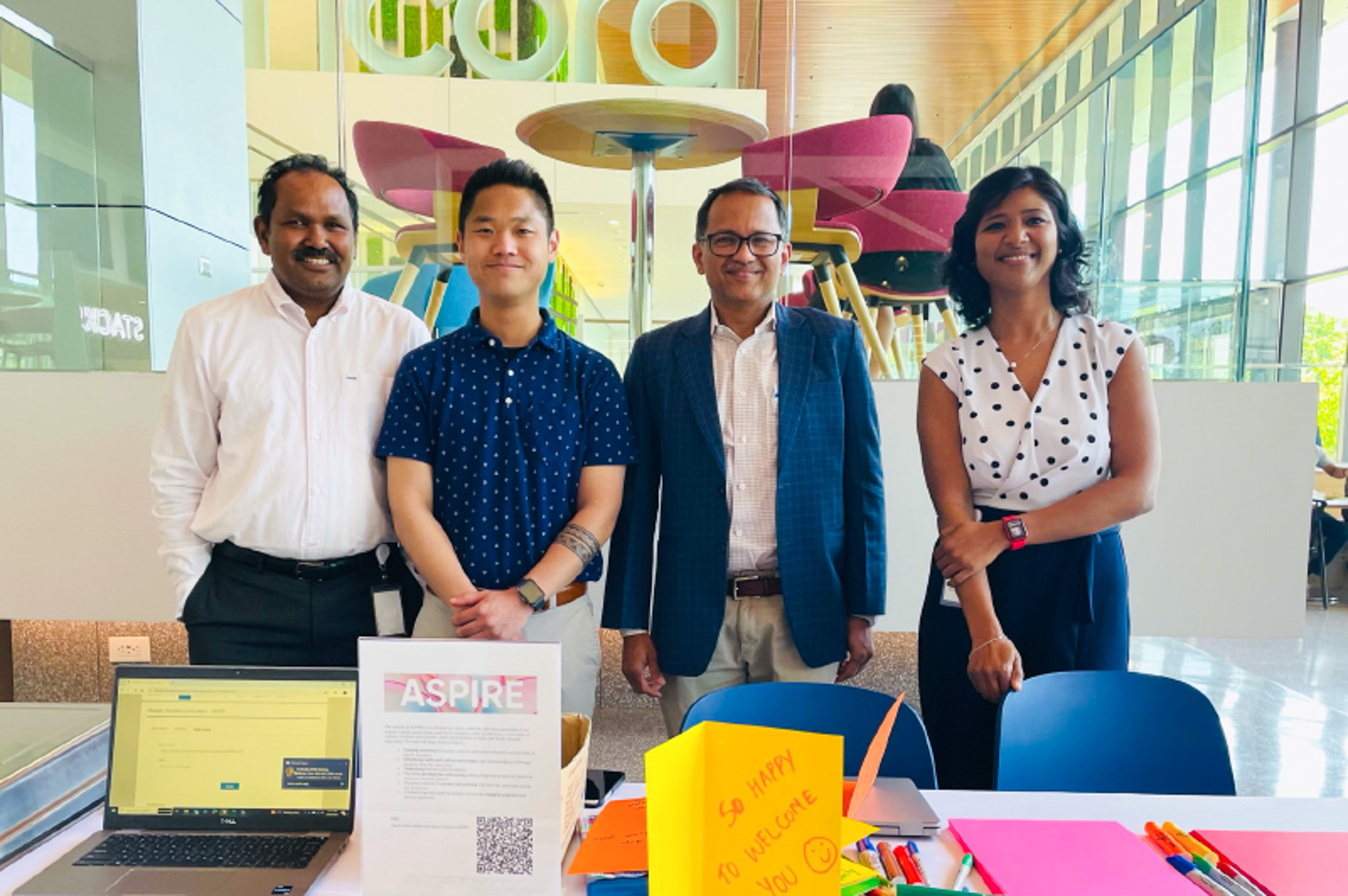 A group of 4 ASPIRE ERG members stand in front of a table with ASPIRE materials on it and pose for a photo at our Cencora headquarters.