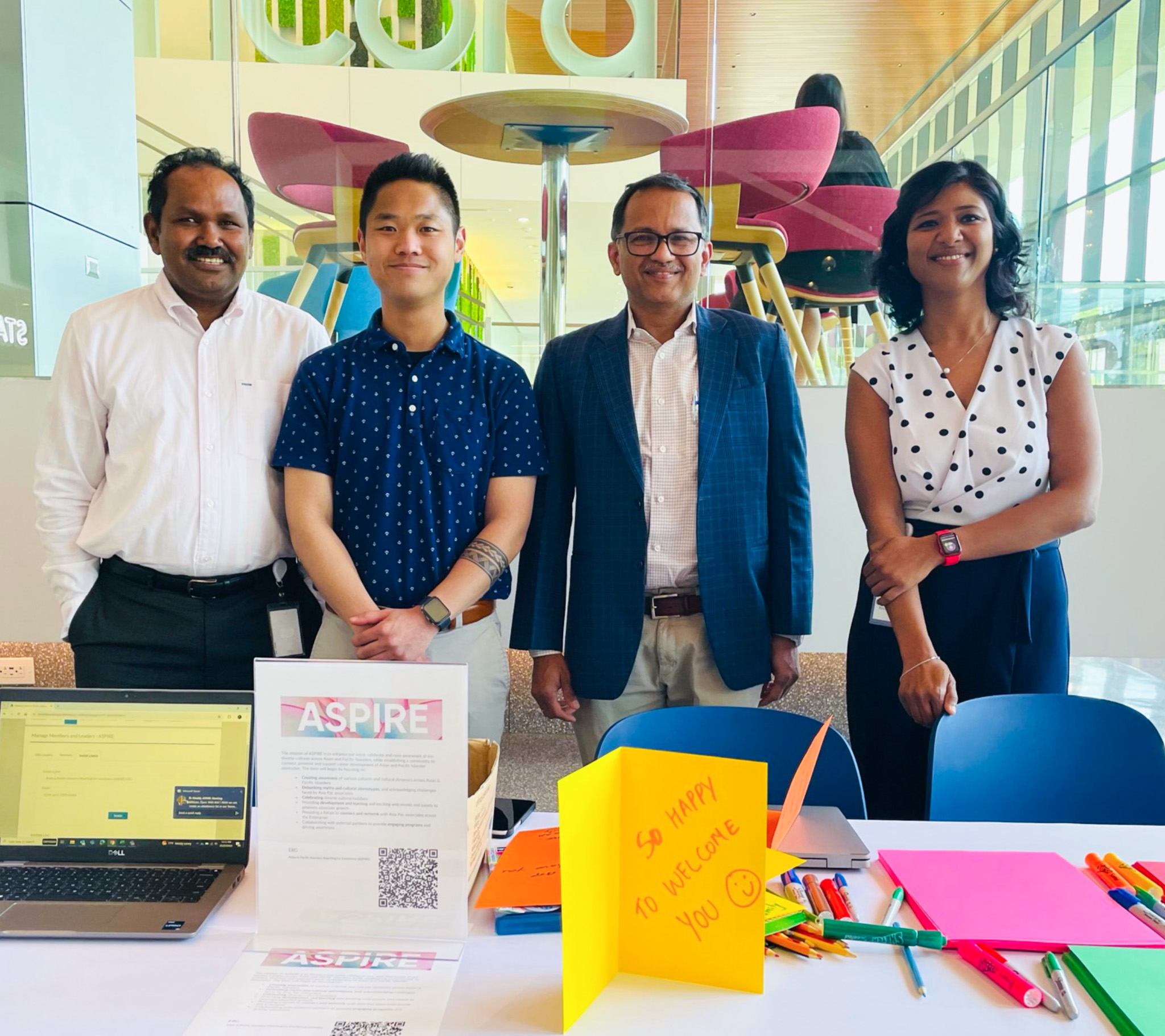 A group of 4 ASPIRE ERG members stand in front of a table with ASPIRE materials on it and pose for a photo at our Cencora headquarters.