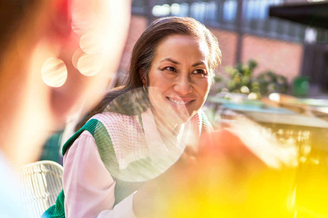 A woman is smiling while seated outdoors.