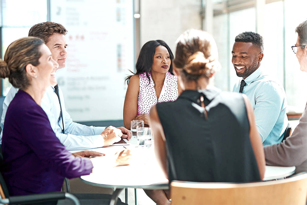 A diverse group of six business professionals casually sitting around a table in an open area.