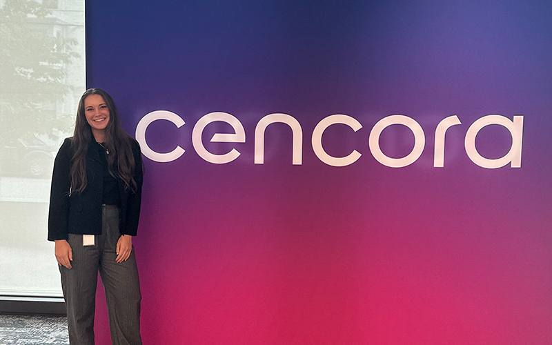 A Cencora intern smiles and poses in front of a Cencora sign.