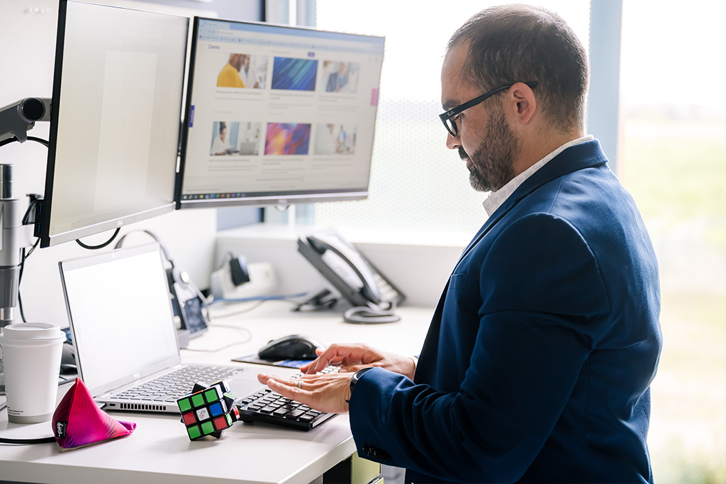 A Cencora team members stands at their desk and is working from multiple monitors in a bright naturally lit space,