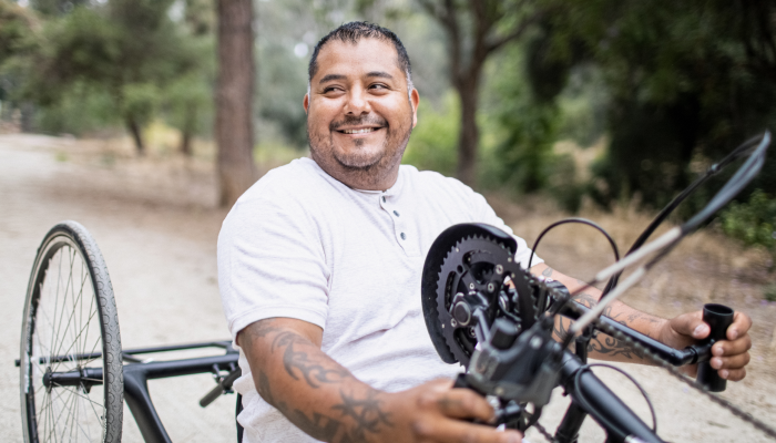 A man rides an adaptive bicycle on a wooded road.