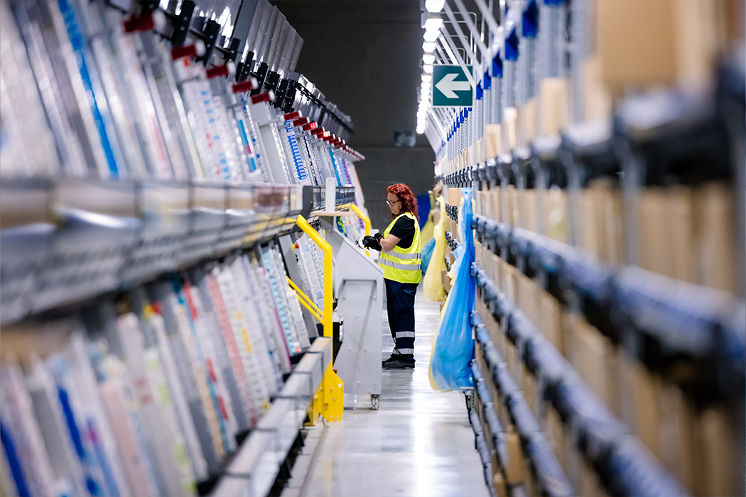 A Cencora team member stands in a distribution center taking stock. They are wearing a high visibility vest.