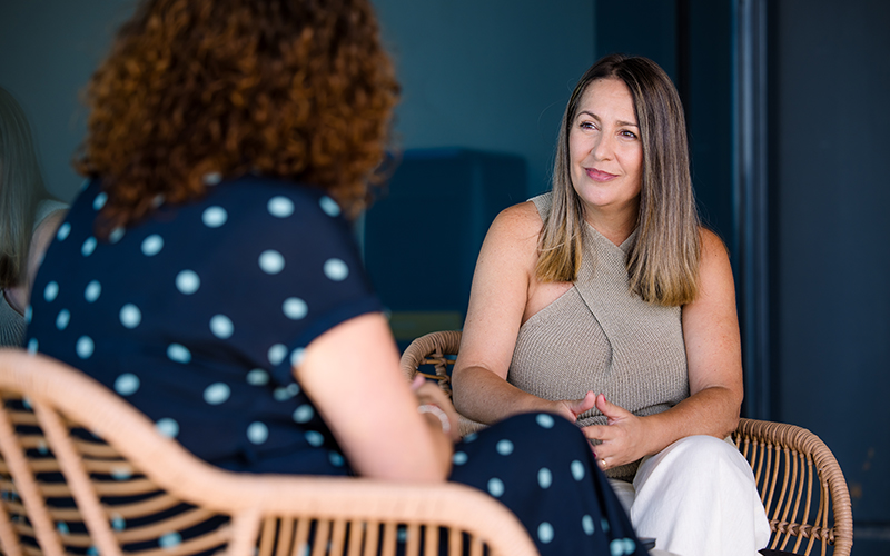 A Cencora team member sits in a rattan chair in a shared office space, opposite of another Cencora team member.