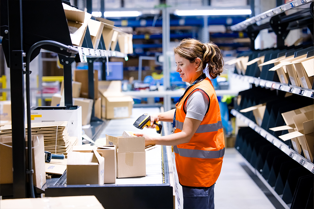 A Cencora team member works by scanning packages and labels in a warehouse setting. They are wearing a high visibility vest.