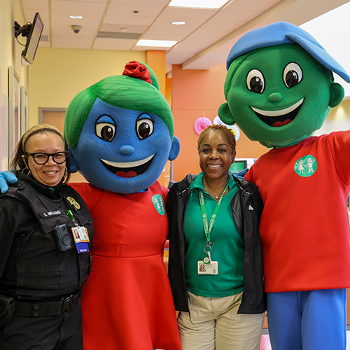 A security officer and registration staff member stand with Children’s mascots, Hope and Will, during an employee recognition event at our Urgent Care Center.