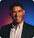 A man with a cleft chin wearing a gray button down under a gray checked suit jacket smiles at the camera.