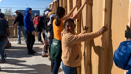 Volunteers helping to build a structure. A line of people are holding up a wall.