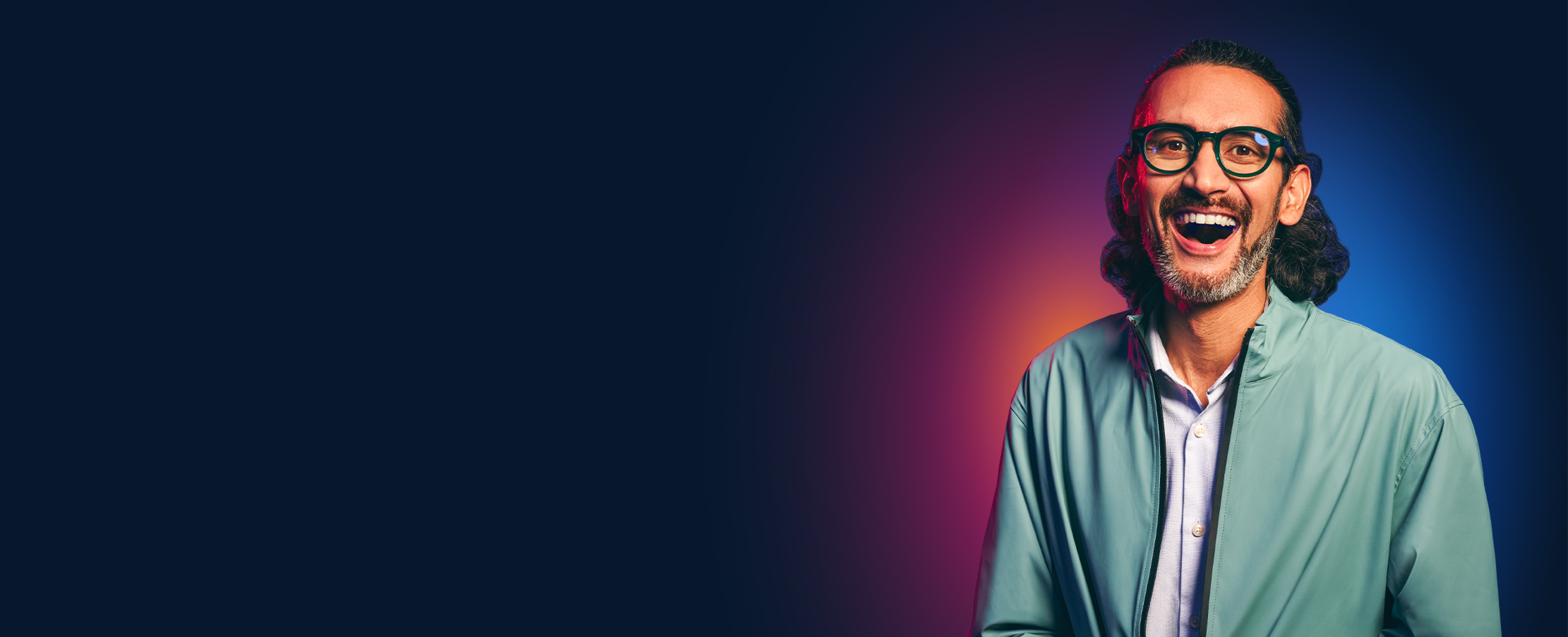 A man wearing glasses and a mint green jacket laughs heartily.