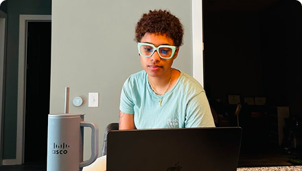 A young woman in glasses looks down at a computer.