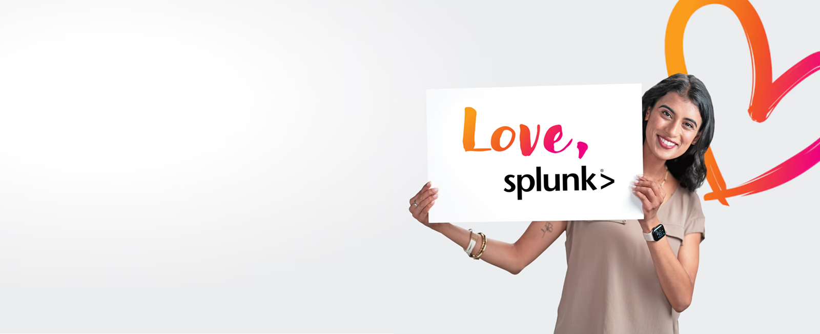 A smiling woman stands in front of a drawn heart holding a Love, Splunk sign.