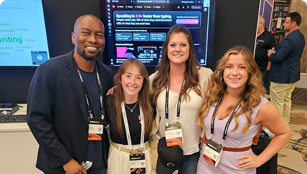 Four people stand in front of a display screen wearing badges at a professional event.