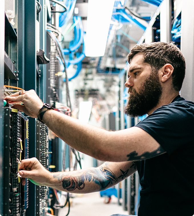 A bearded man works hands-on on server connections in a data center.