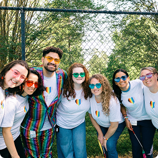 A group of smiling Cisconians outside at an event wearing heart sunglasses and rainbow heart t-shirts.