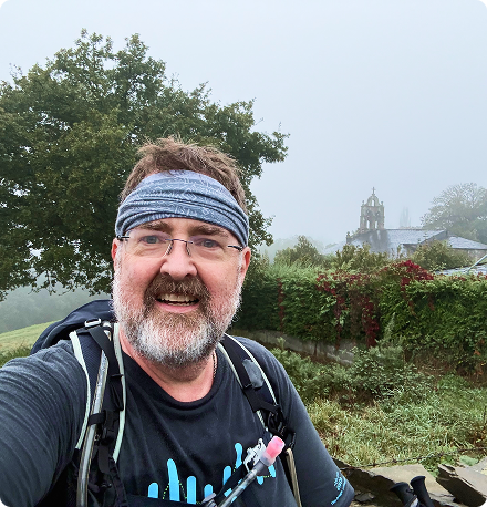 A man wearing a headband and glasses takes a selfie on a bike ride.
