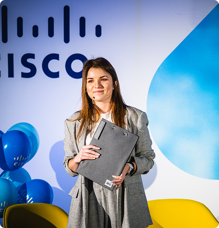 A woman holding a clip board stands in front of a Cisco backdrop.