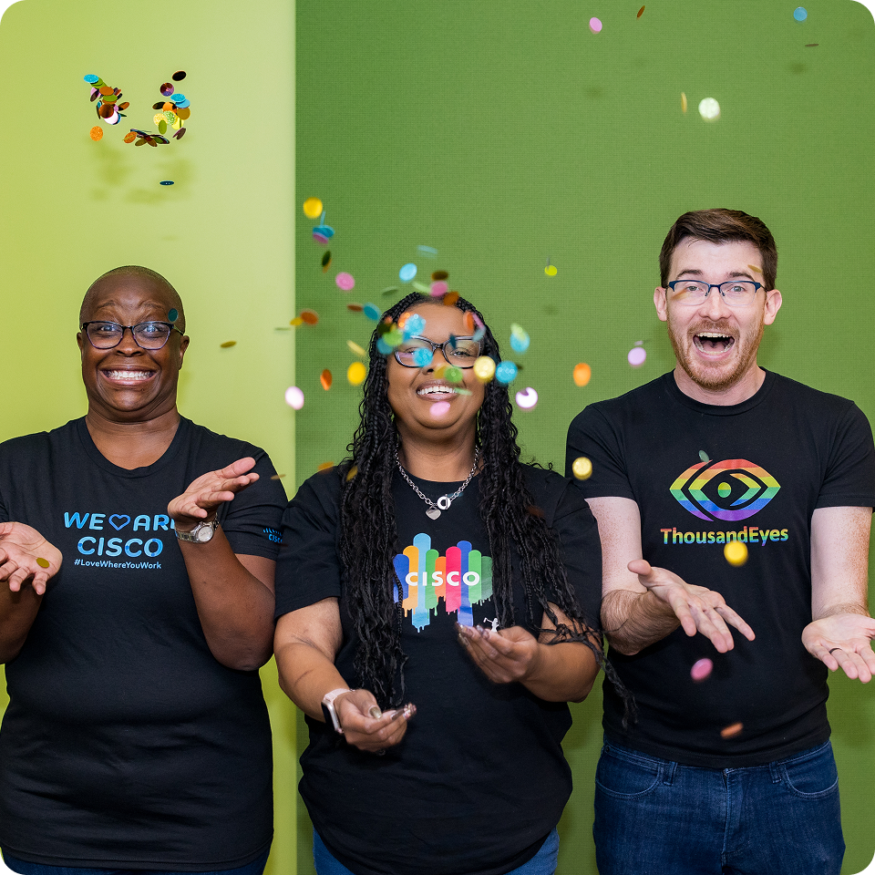 Three people excitedly toss confetti in the air wearing Cisco and ThousandEyes Pride t-shirts.