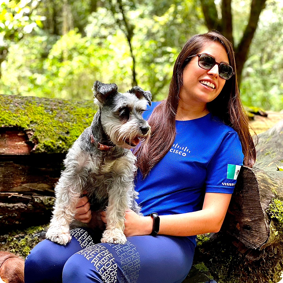 A smiling woman sits on a log with her dog on her lap.