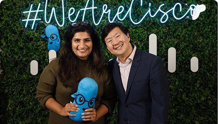 Avini stands with actor Ken Jeong  in front of a leafy wall that says "We Are Cisco."
