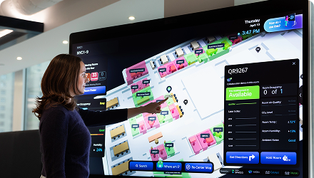 A woman points at a digital screen with a map of available conference rooms.