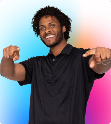 A young Black man wearing a short-sleeved black polo shirt smiles big while pointing both hands directly at the camera.