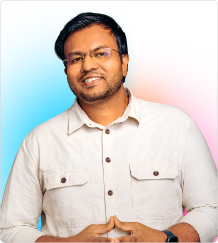 A man wearing an off-white shirt with brown buttons and rimless glasses smiles while holding his hands together in front of his stomach.