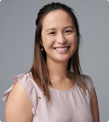 An young woman with shoulder-length hair wearing a white and pink striped blouse with cap sleeves smiles brightly at the camera.
