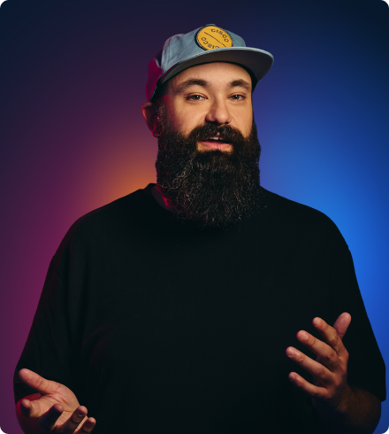A man with a beard wearing a blue baseball cap with a Cisco patch on it talks animatedly with his hands while looking at the camera.