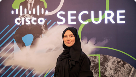 A woman in a hijab standing in front of a Cisco Security backdrop at an event.