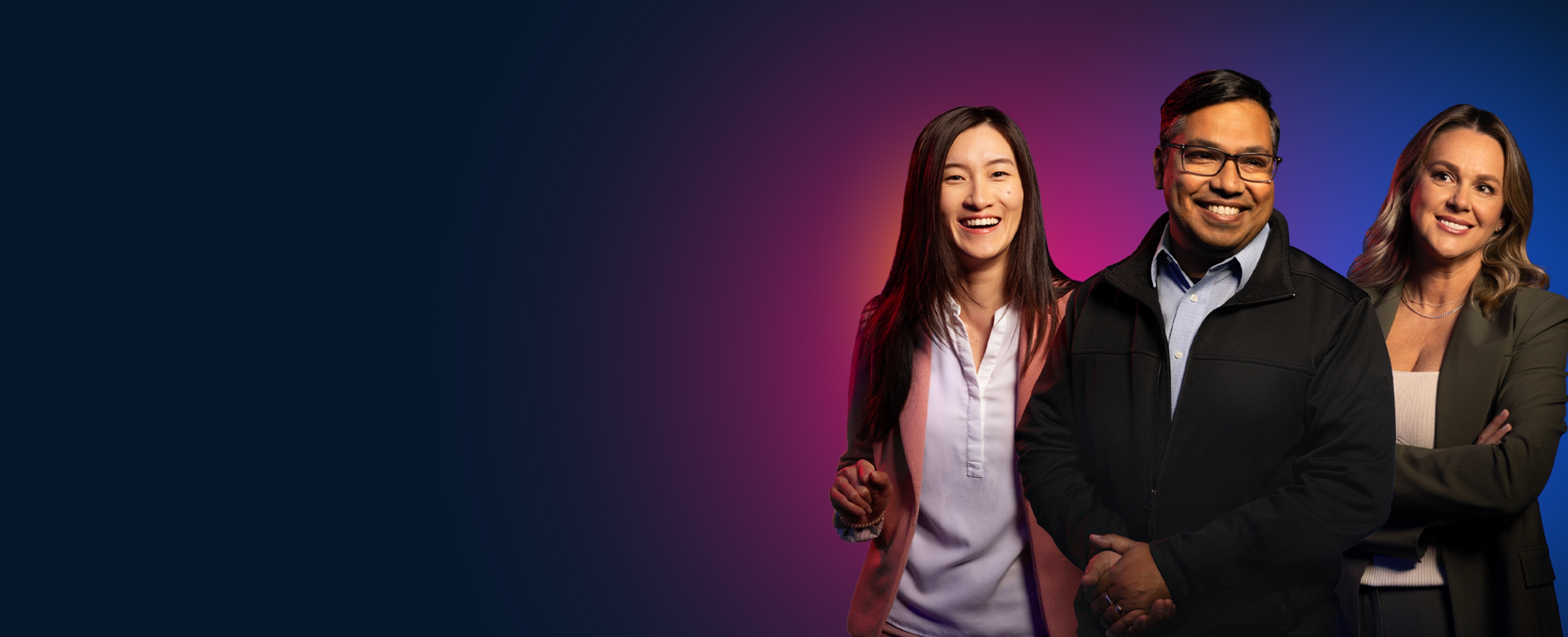 Two smiling women stand on either side of a smiling man wearing glasses.