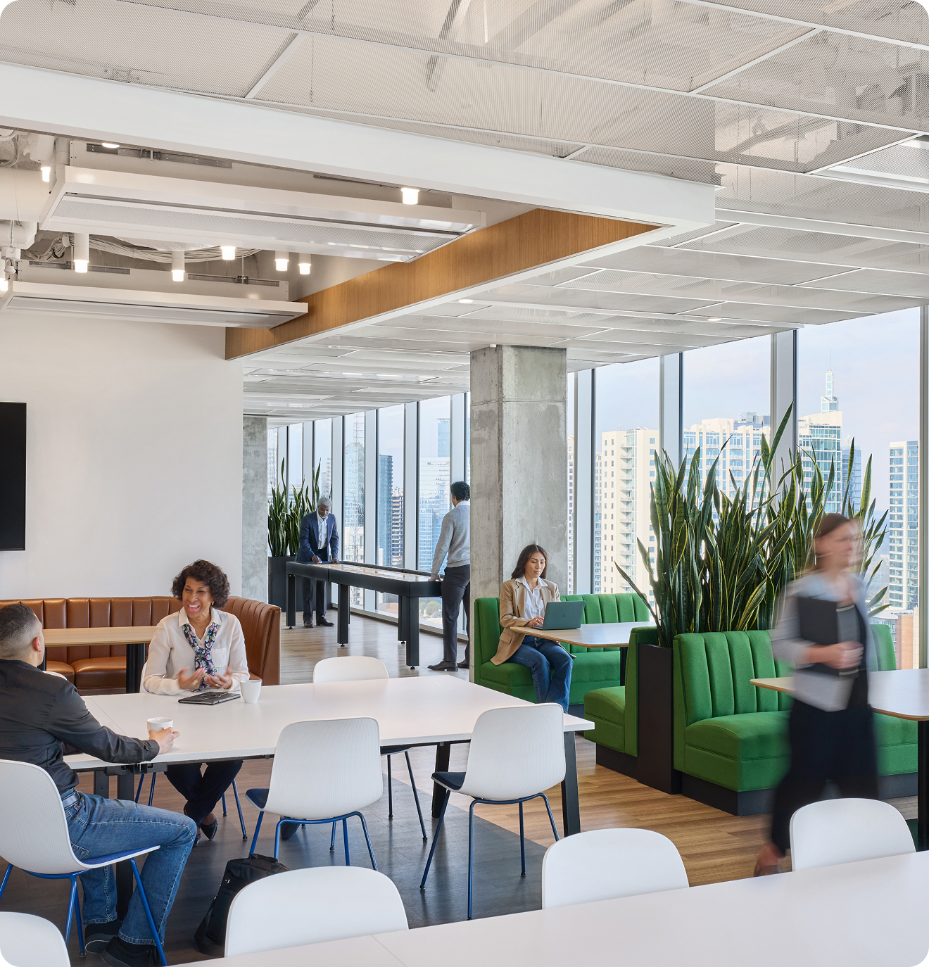 An open working area with people working at different style tables and some playing table shuffleboard.