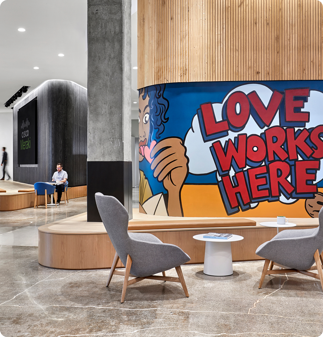 A lobby with blonde wood accents and modern, gray chairs. A mural on the wall says "Love Works Here".