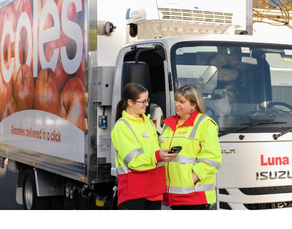 Two female customer delivery drivers working outside the CFC looking at an electronic device and a Coles delivery van parked behind them