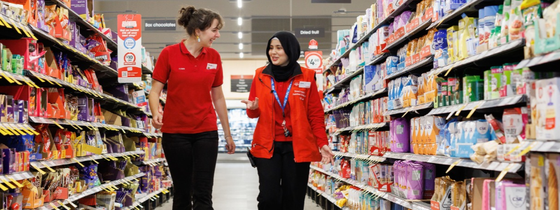Two Coles team members walking and talking in a supermarket aisle